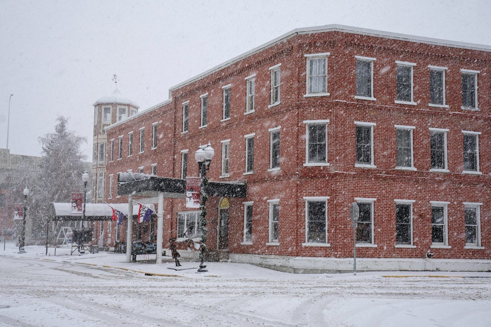 A three-storey red brick commercial block on a street corner during heavy snowfall