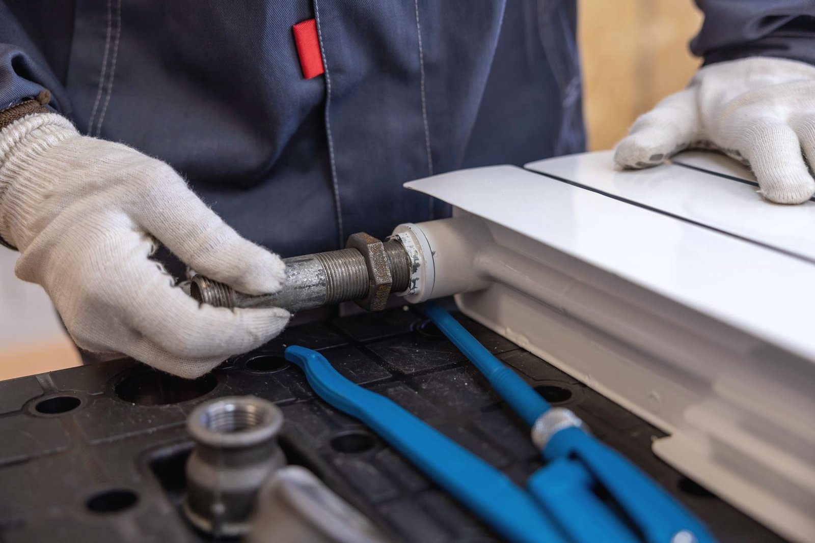 Gloved hands threading a steel nipple into the end of a white panel radiator